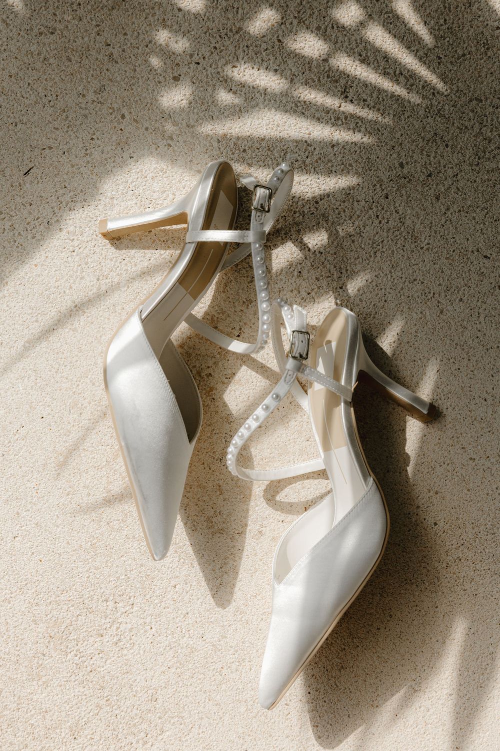 Elegant white strappy high heel shoes with pointed toes casting dramatic shadows in natural light.