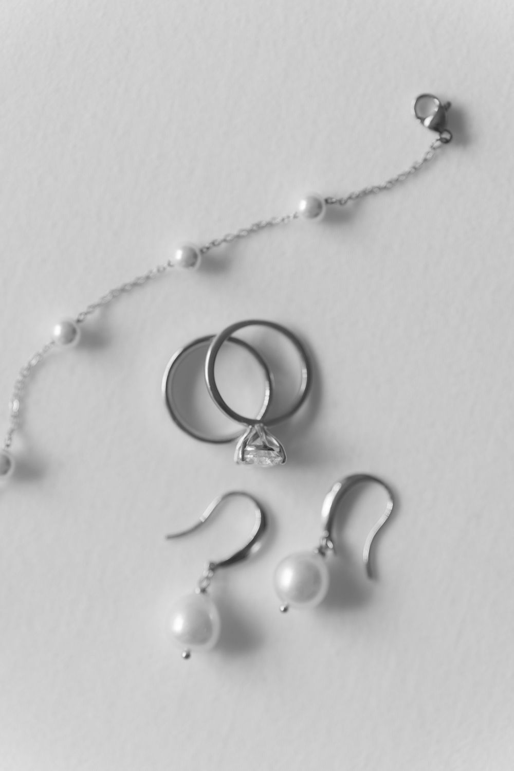 Wedding jewelry arrangement with pearl bracelet, diamond rings, and matching pearl earrings on white background.