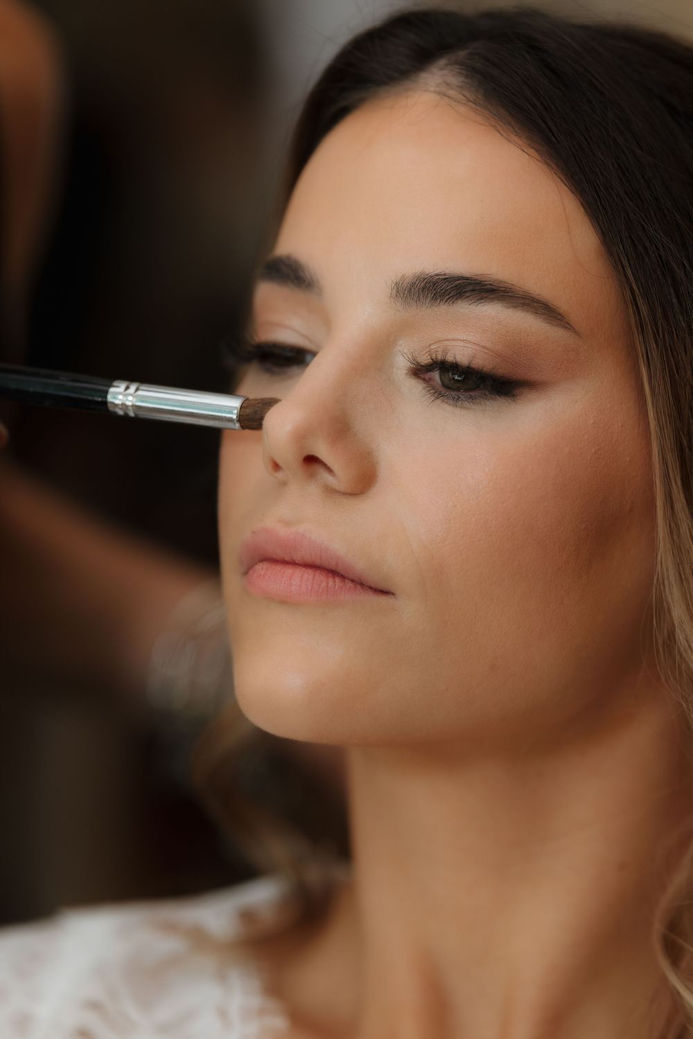 Close-up shot of bridal makeup application with a brush on a woman with naturally glowing skin.