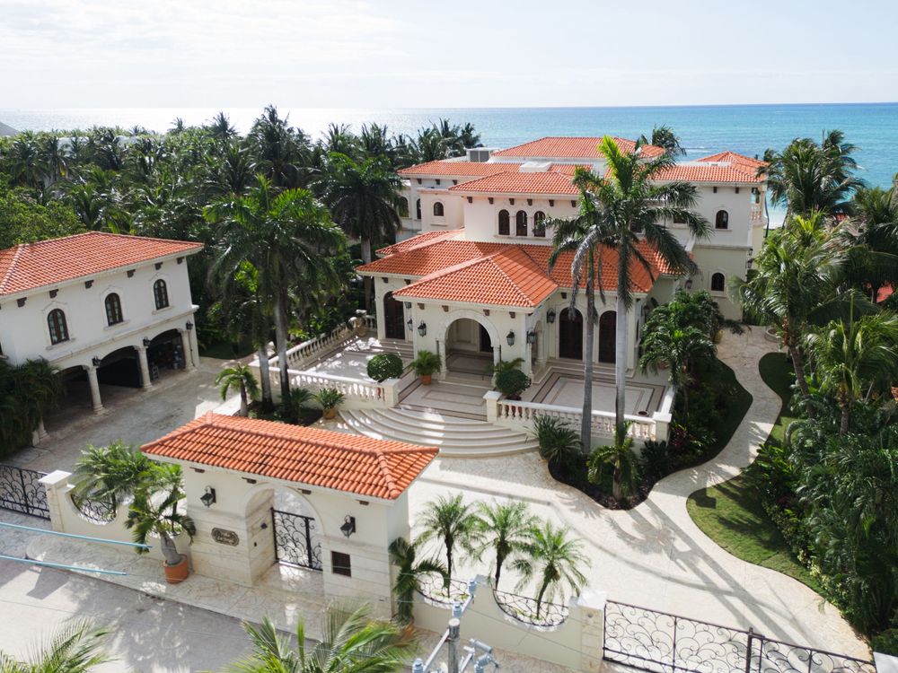 Aerial view of luxurious Mediterranean-style villa with terracotta roofs and palm trees near the ocean.