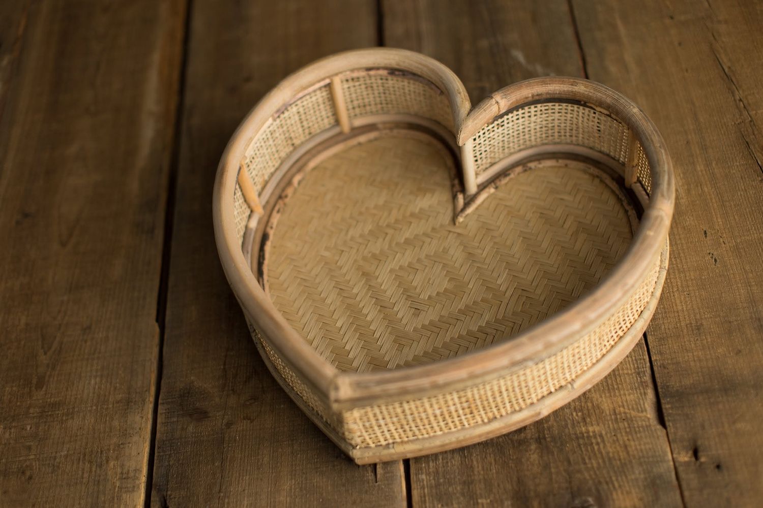 Heart-shaped woven rattan basket with burlap lining on rustic wooden background.