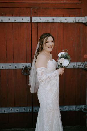 A bride holds a white floral bouquet while posing in front of vintage wooden doors.