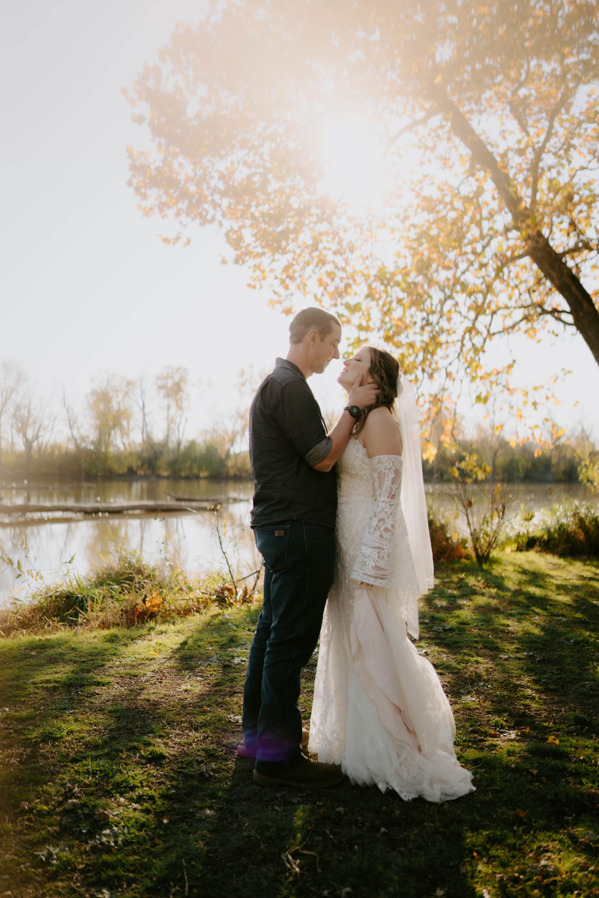 Newlyweds share a romantic moment in golden autumn sunlight by a lake.