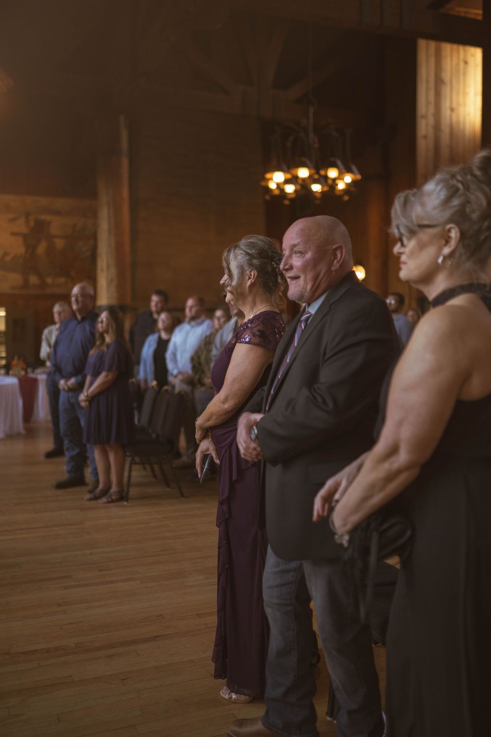 Wedding reception guests slow dancing in a dimly lit rustic venue.