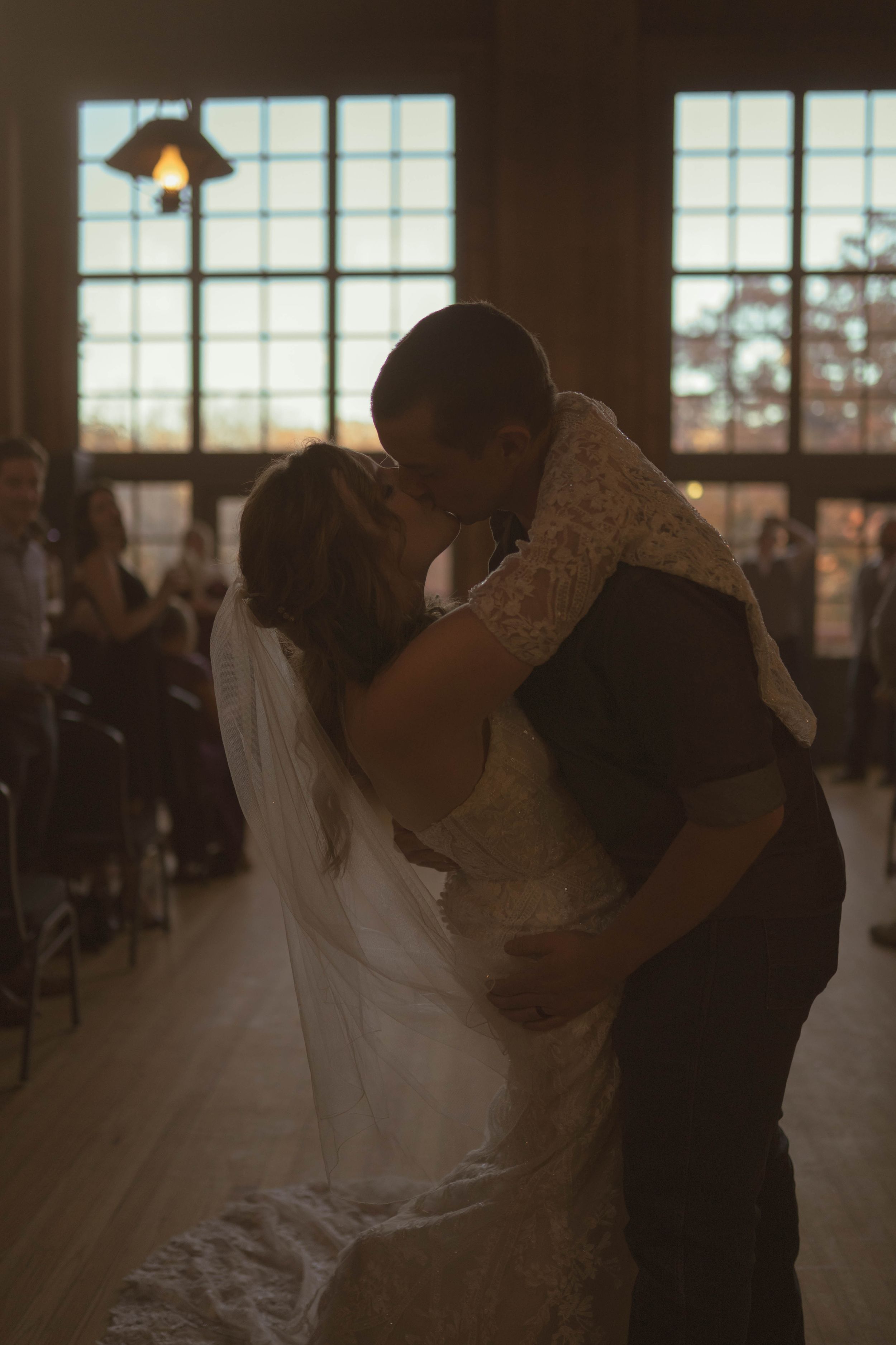 Romantic first dance silhouettes in a rustic wedding venue with window light.