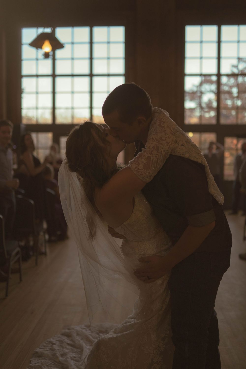 Romantic first dance silhouettes in a rustic wedding venue with window light.