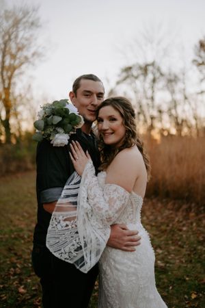 Autumn wedding portraits with couple embracing among fallen leaves at sunset.