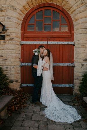 A couple poses against rustic red wooden doors and stone archways during their wedding photoshoot.