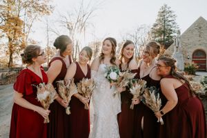 Wedding party in burgundy and neutral attire poses together during fall outdoor ceremony.