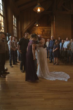 Wedding guests gather on wooden dance floor inside rustic barn venue with pendant lighting.