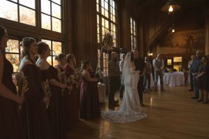 Wedding ceremony in progress inside rustic wooden venue with natural light streaming through windows.