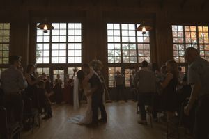 Wide view of wedding ceremony inside rustic venue with large windows and natural lighting.