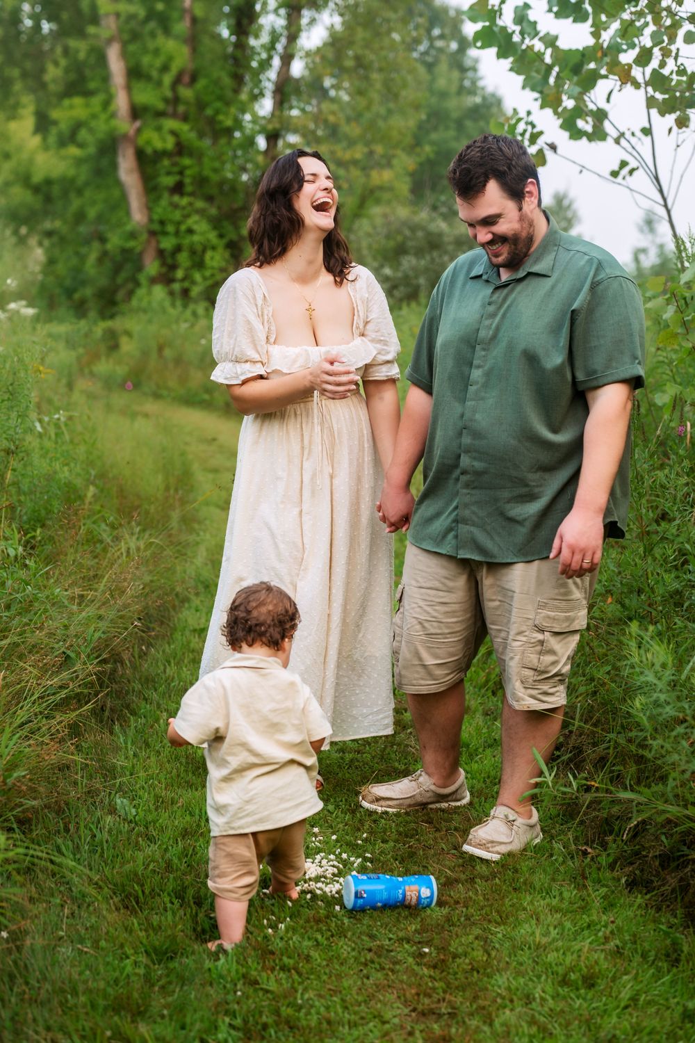 Family walking and laughing together in casual clothes through green summer meadow.