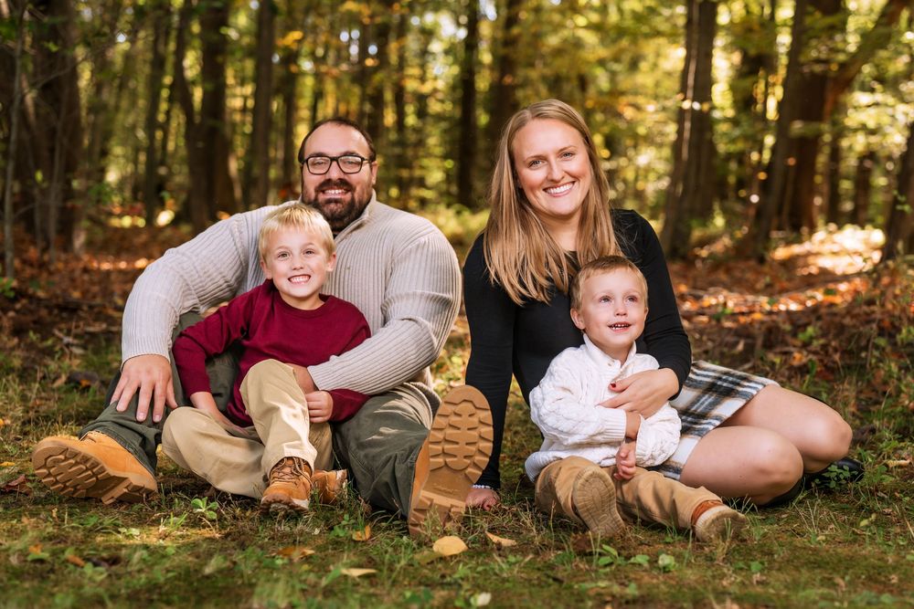 Family relaxing together on fallen leaves in wooded autumn setting.