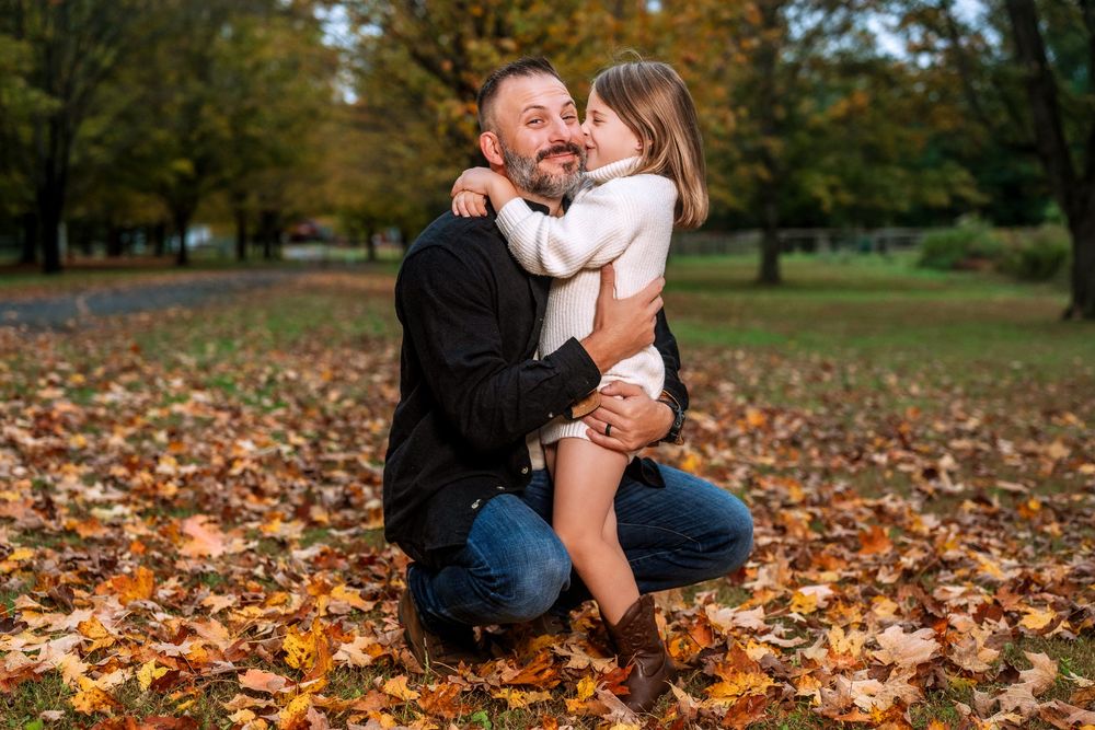 Family enjoying tender moments together on ground covered with fall foliage.