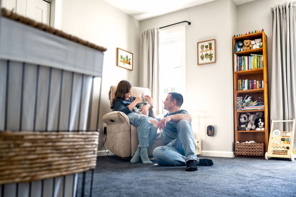 Father and child playing together in a cozy carpeted bedroom with a bookshelf and recliner chair.