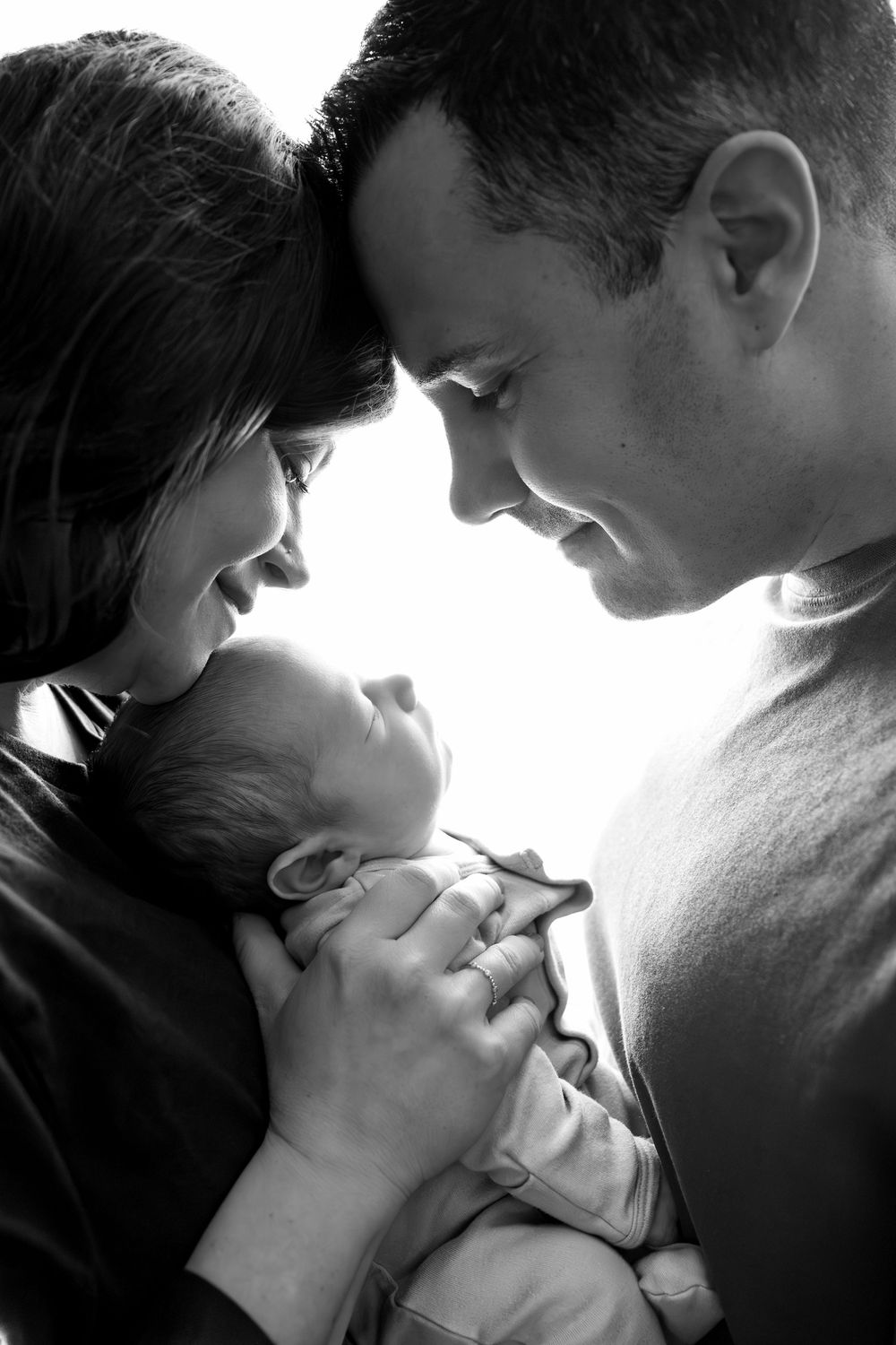 Black and white photo of smiling parents tenderly holding their newborn baby close together.
