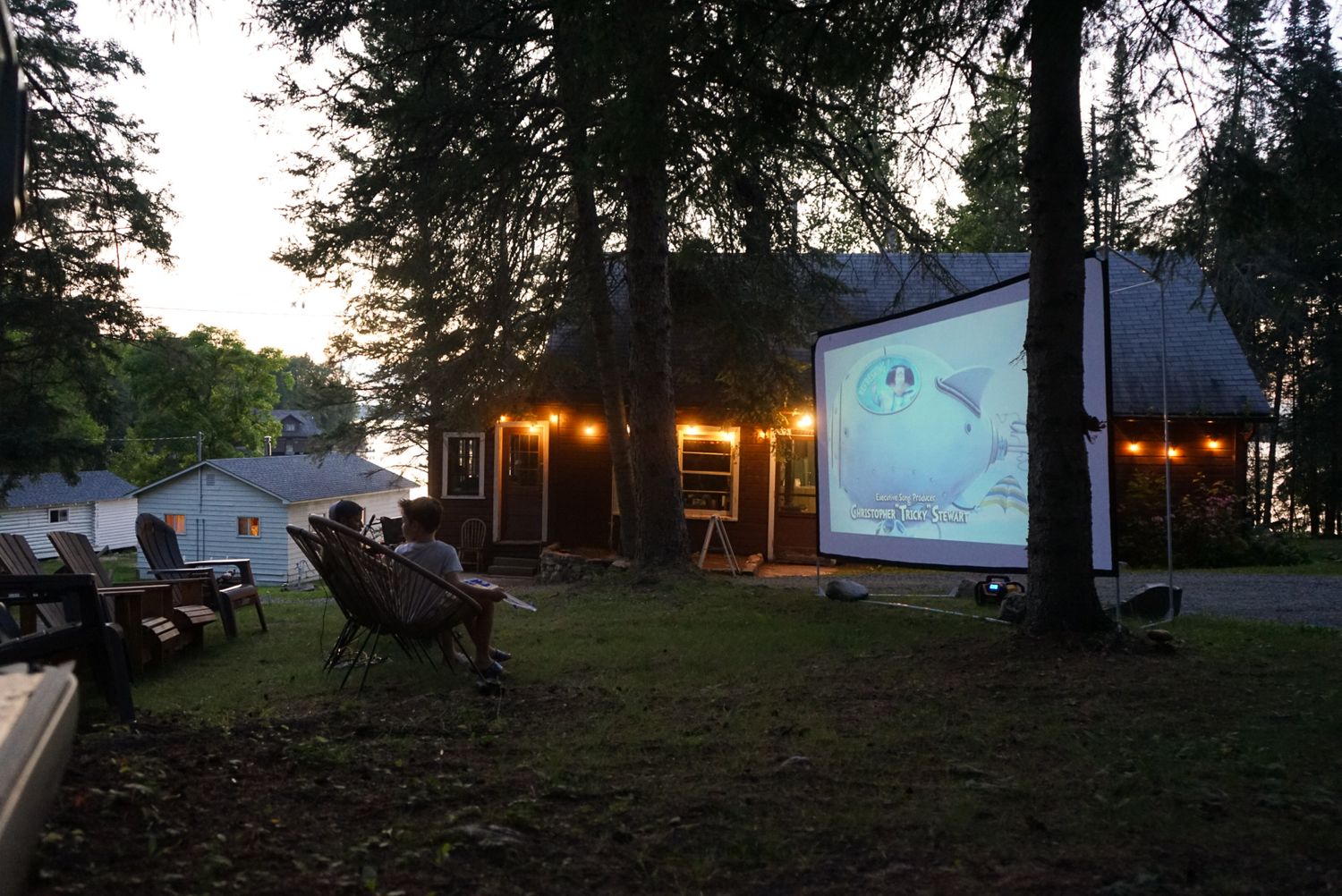 Outdoor movie screening setup at dusk with trees and projection screen.