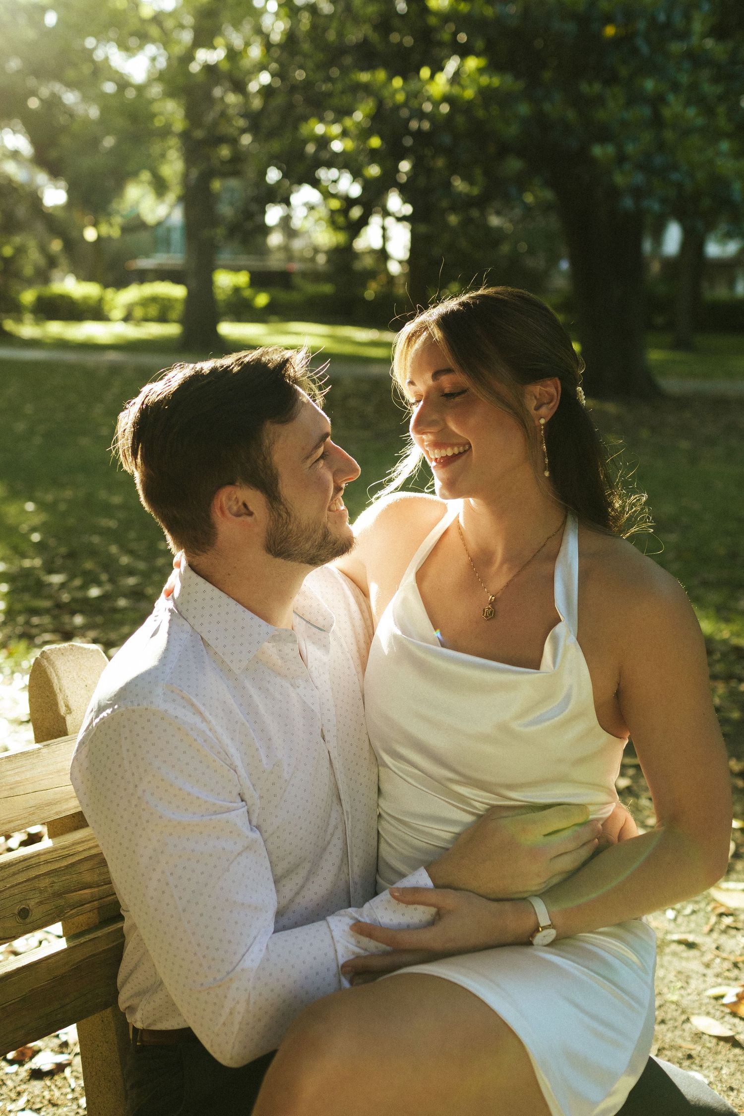 A couple on a bench at Forsyth Park in Savannah smiling at each other with golden light silhouetting their faces