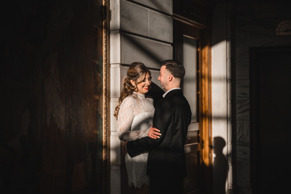 Romantic wedding couple sharing an intimate moment in a dimly lit hallway with dramatic shadows.