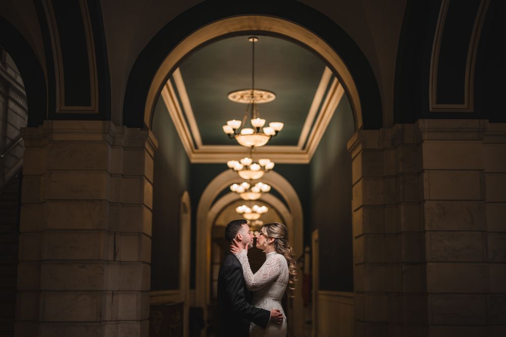 Wedding couple embracing under ornate arched ceiling with crystal chandeliers.