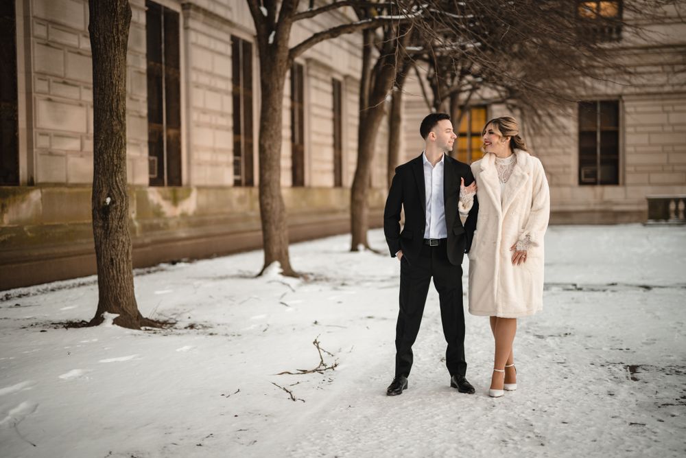 Couple walking through snow-covered grounds of historic stone building.