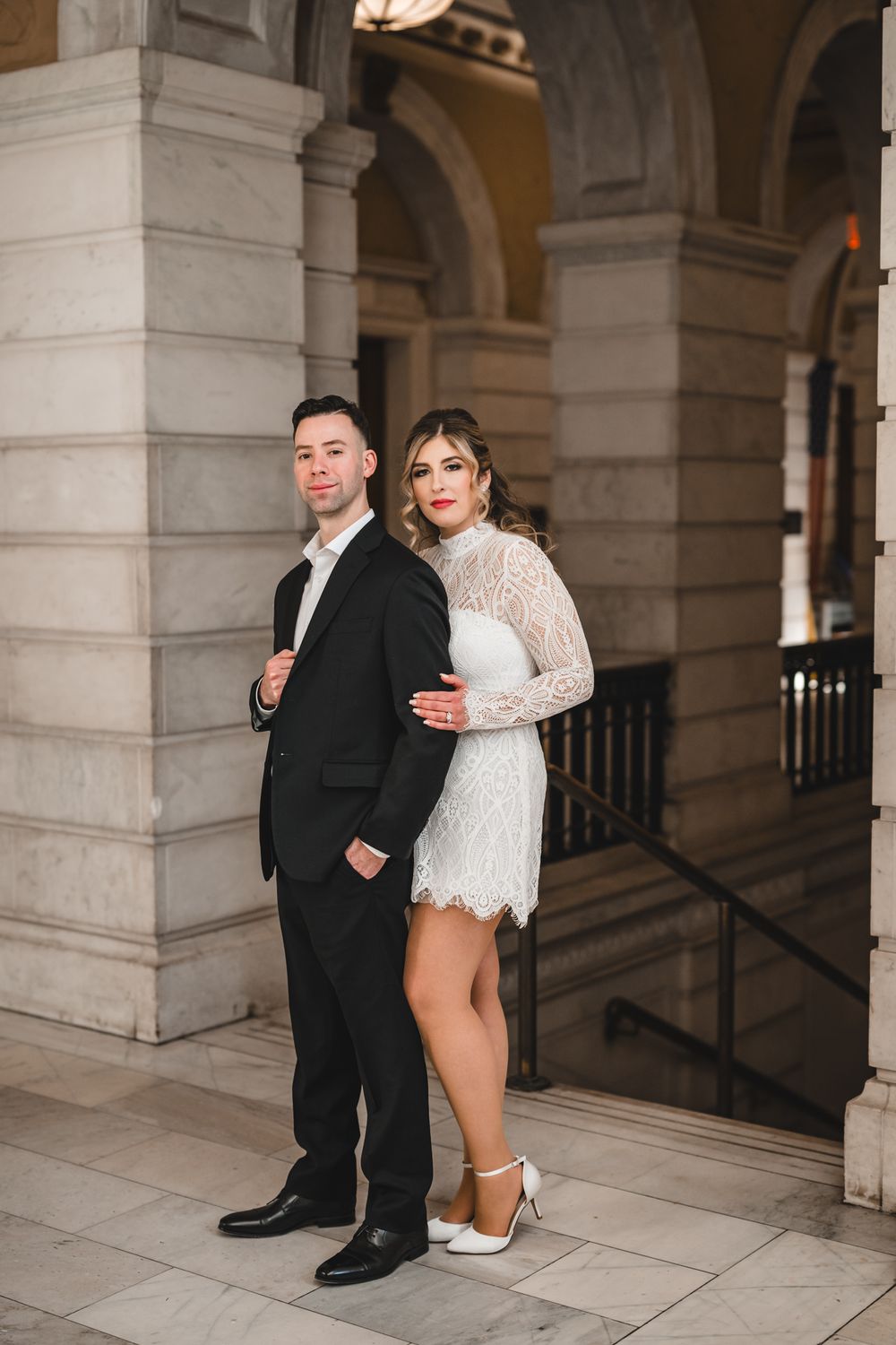 A couple poses playfully in an elegant colonnade with stone pillars and arches.