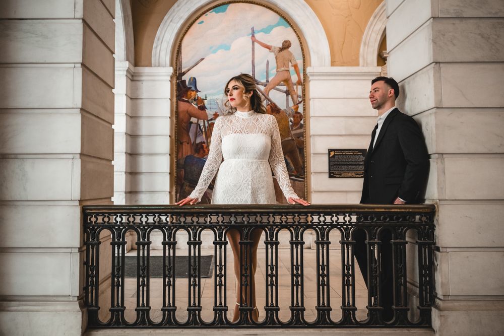 Couples pose along an ornate colonnade with arched windows and decorative railings.
