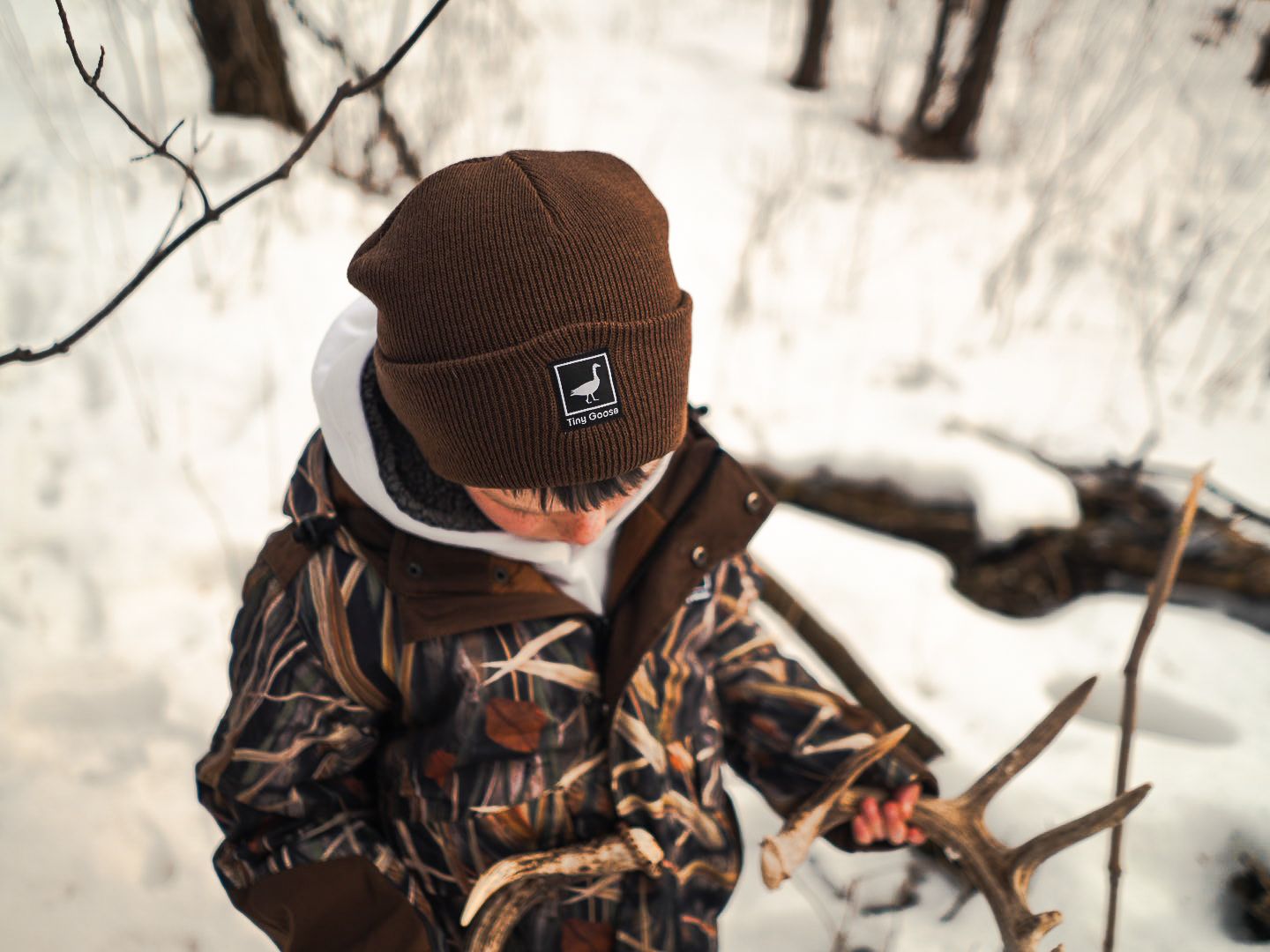 Person wearing brown beanie and camo jacket in snowy winter forest.