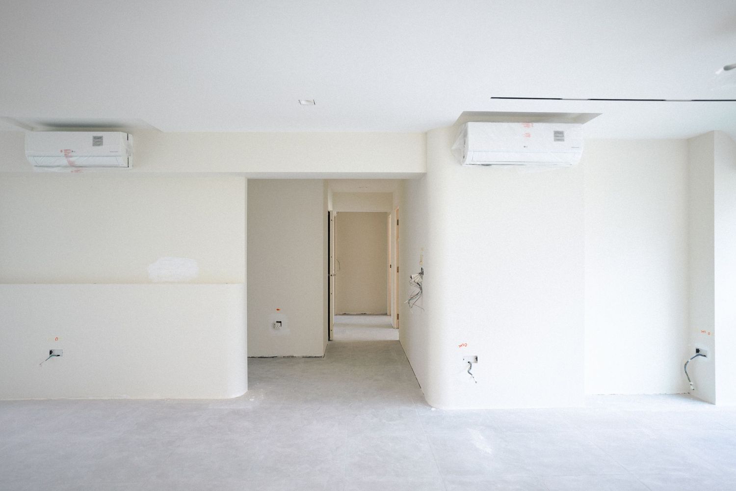 Empty white interior room with air conditioning units mounted on wall and a doorway visible in the distance.