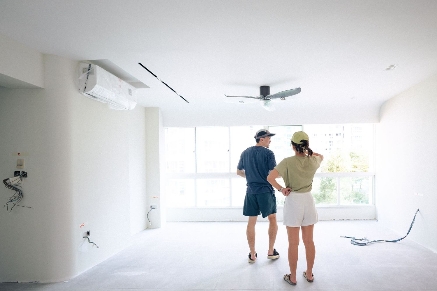 Two people standing in empty white room looking at bare walls while planning renovation together.