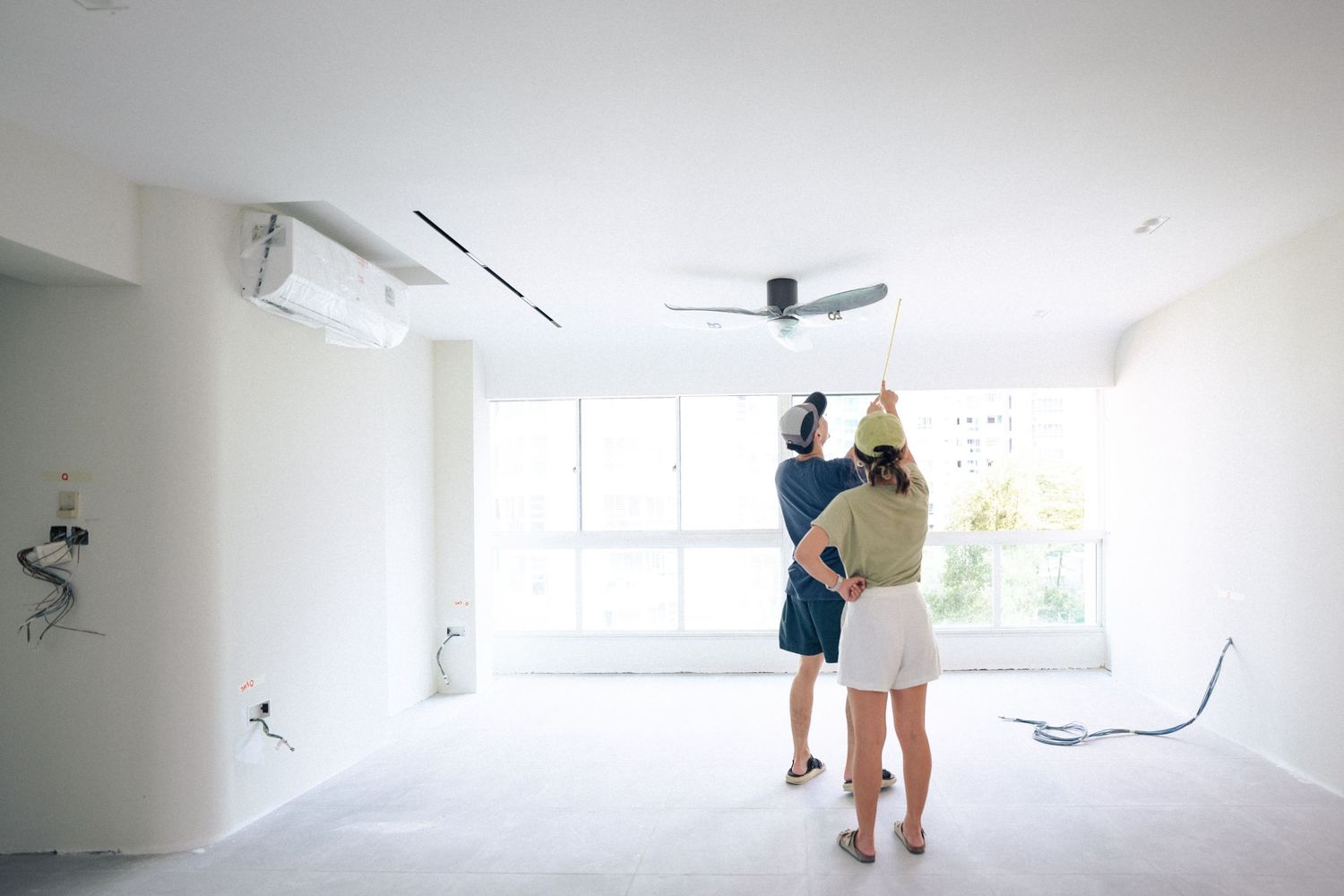 Two people discussing renovation plans in bright empty room with white walls and ceiling fan.