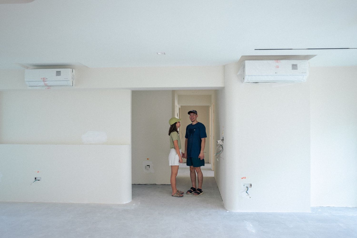 Two figures stand in a doorway between white walls with air conditioning units mounted above.