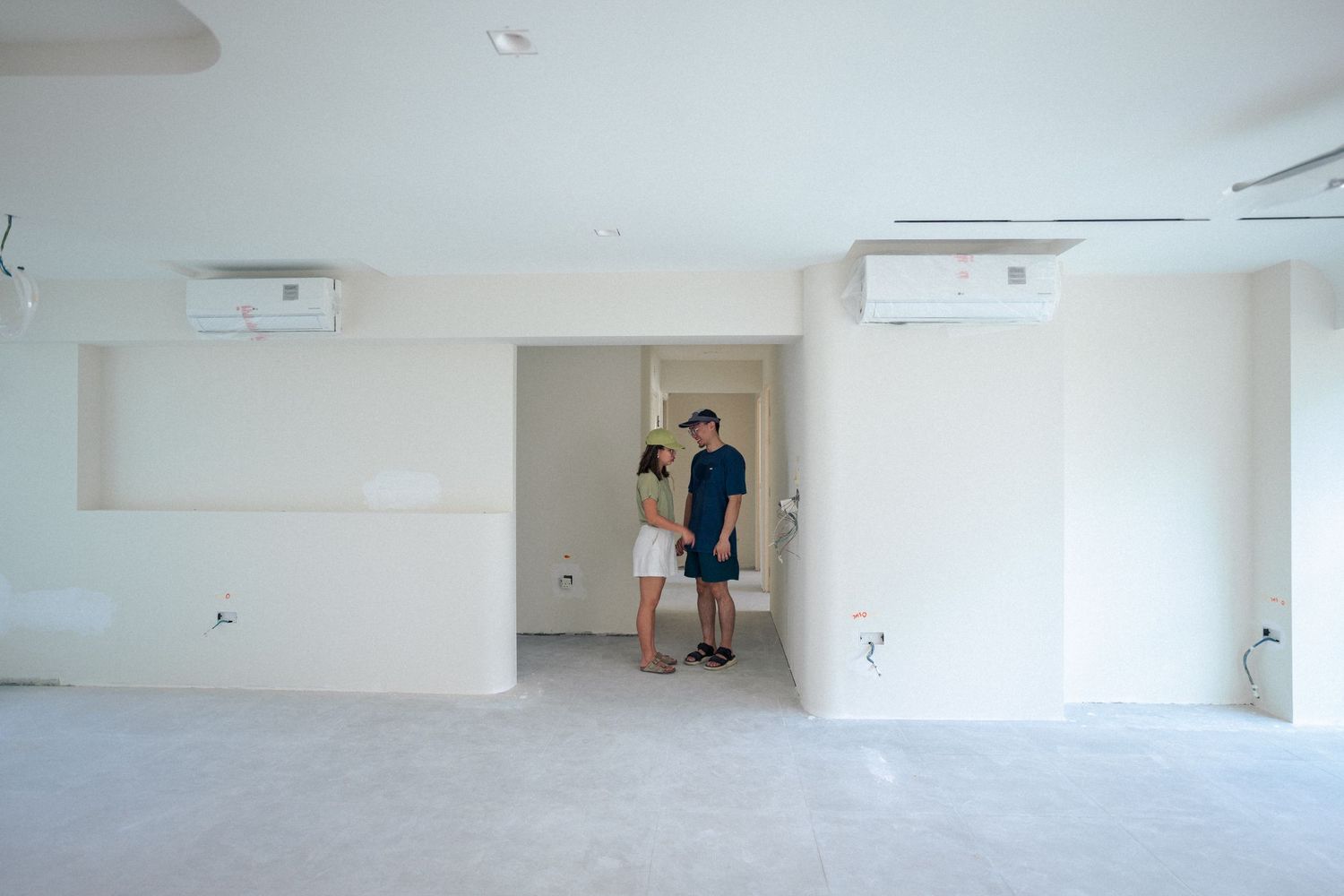 Empty white room interior with mounted air conditioning units and figures standing in doorway.