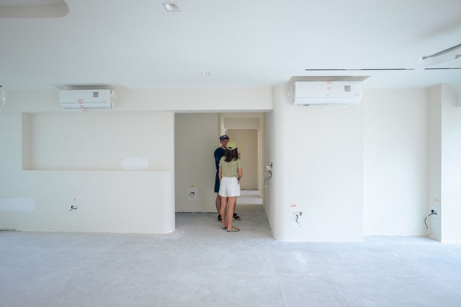 Person in casual attire stands in doorway of empty white room with mounted air conditioning units on wall.