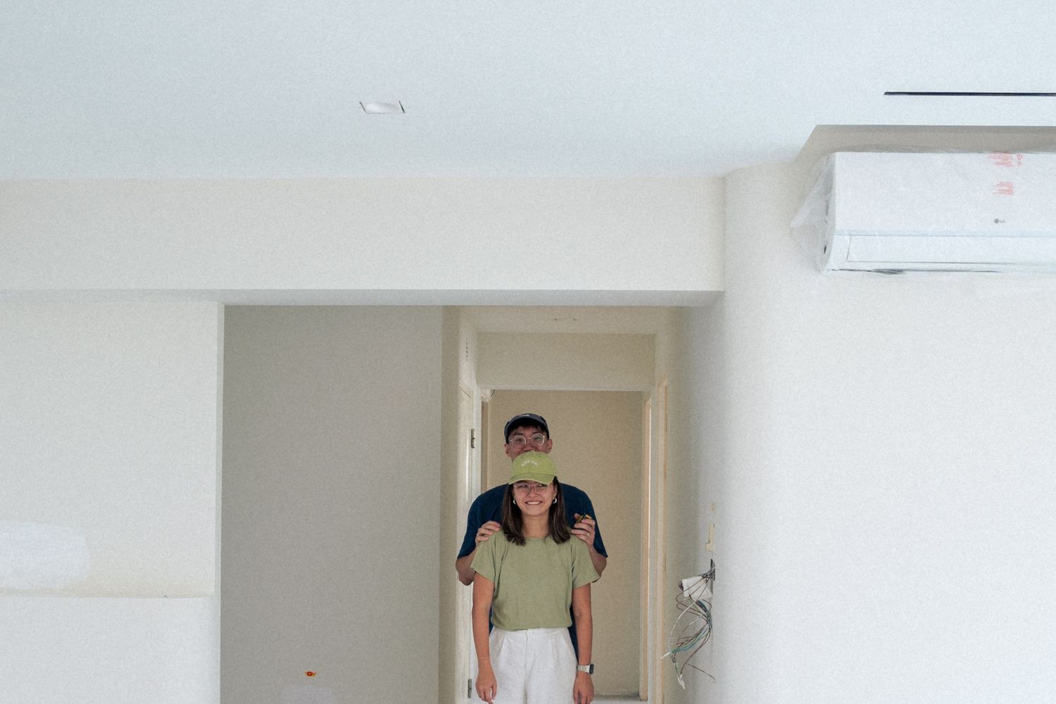Figure in a beige polo shirt and white pants stands in a doorway beneath a wall-mounted air conditioning unit.