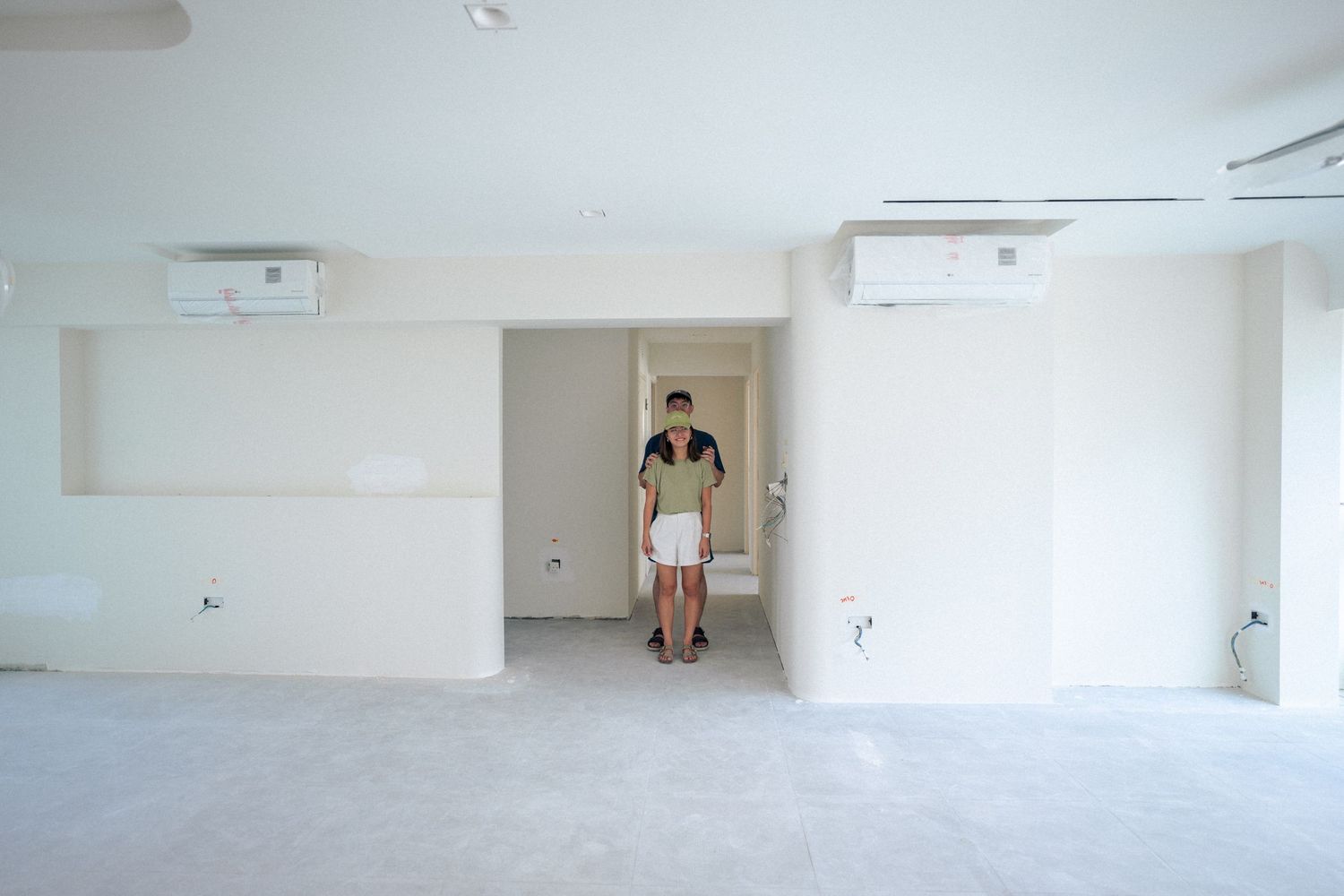 A person standing in a minimalist white empty room with AC units mounted on the wall.
