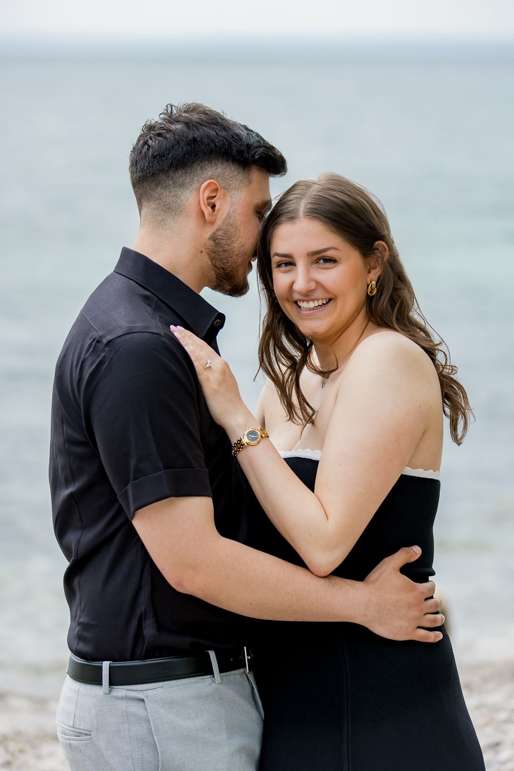 Joyful couple embracing after beach proposal with lake backdrop.