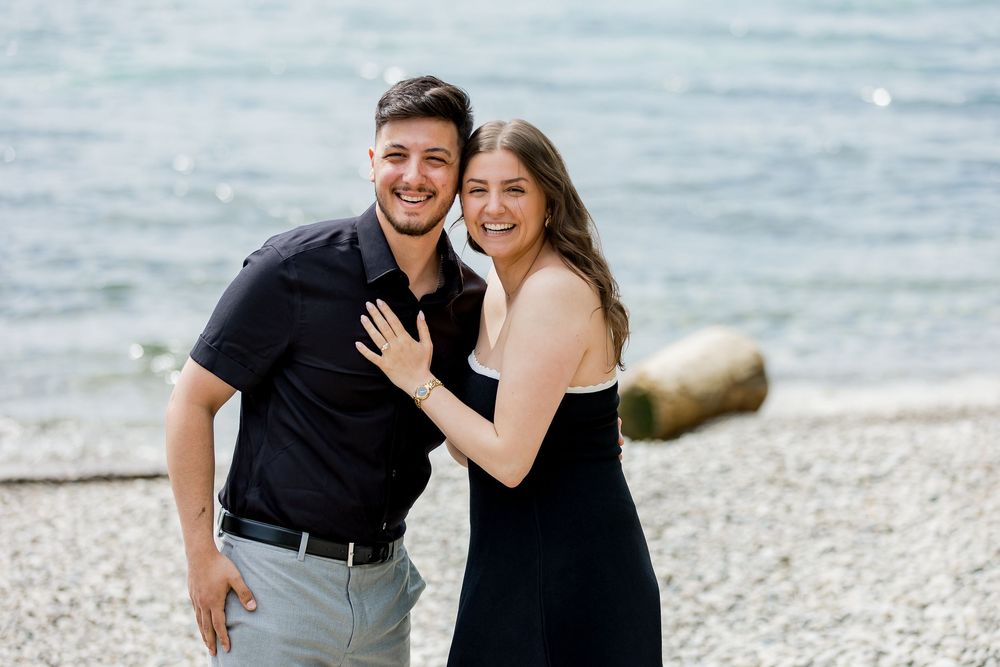 Happy couple celebrating engagement moment on beach shoreline.
