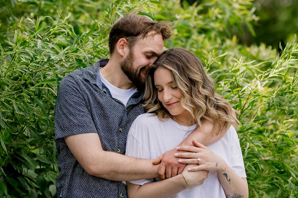 Affectionate couple sharing an intimate moment among lush green foliage in natural lighting.