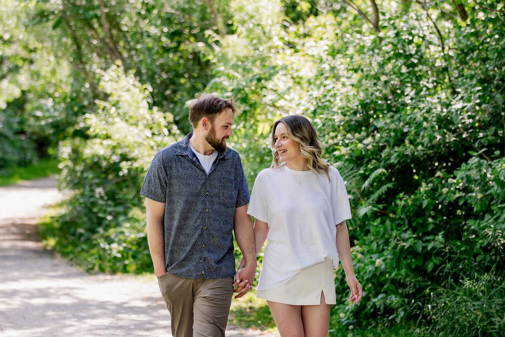 A couple walking hand in hand along a sunny garden path surrounded by blooming white flowers and lush greenery.