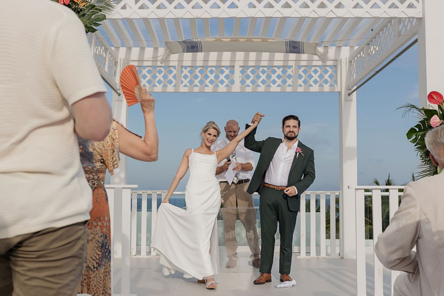 A wedding celebration under a white gazebo with guests waving and clapping at an outdoor venue.