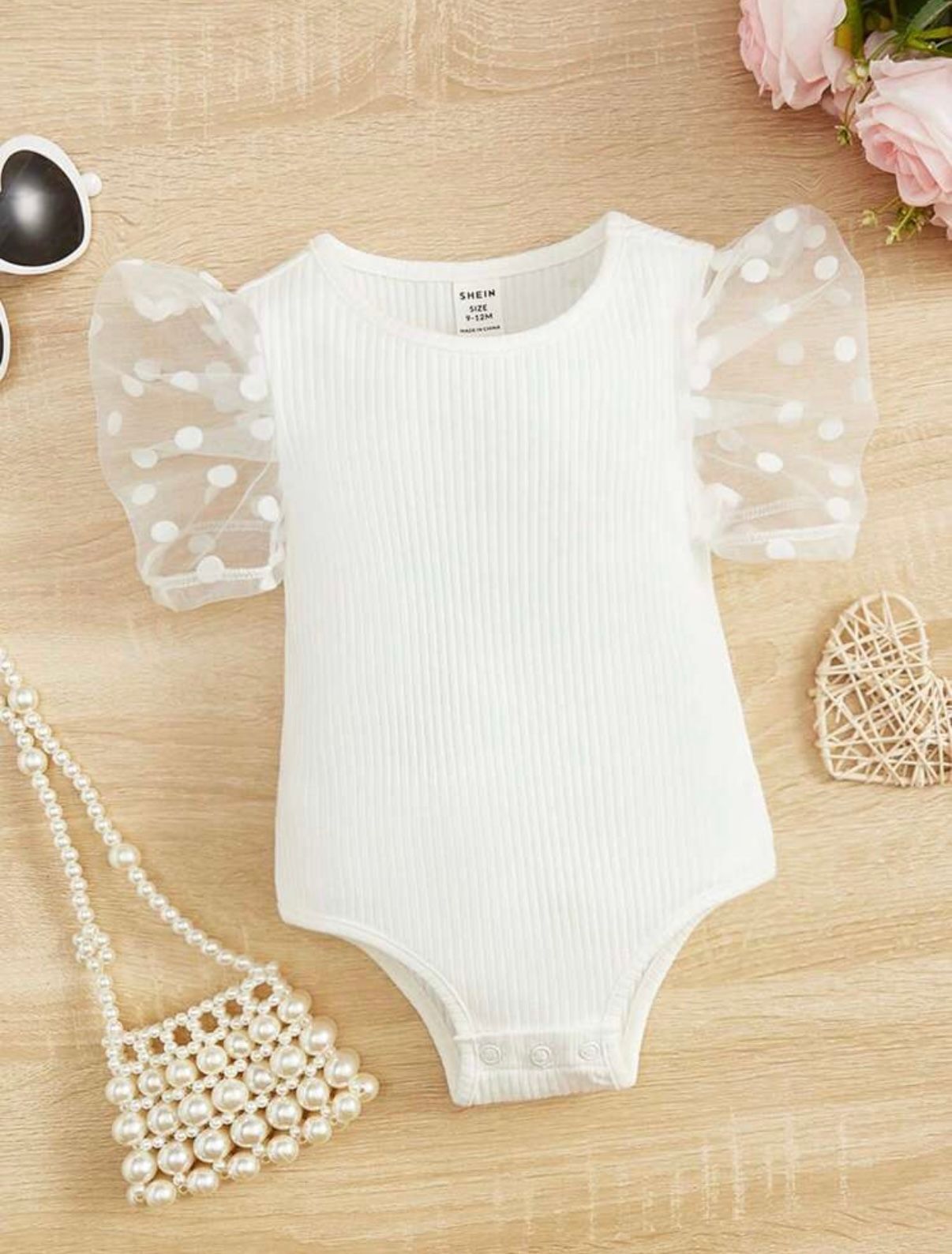 White ribbed bodysuit with sheer sleeves displayed with pearl accessories.