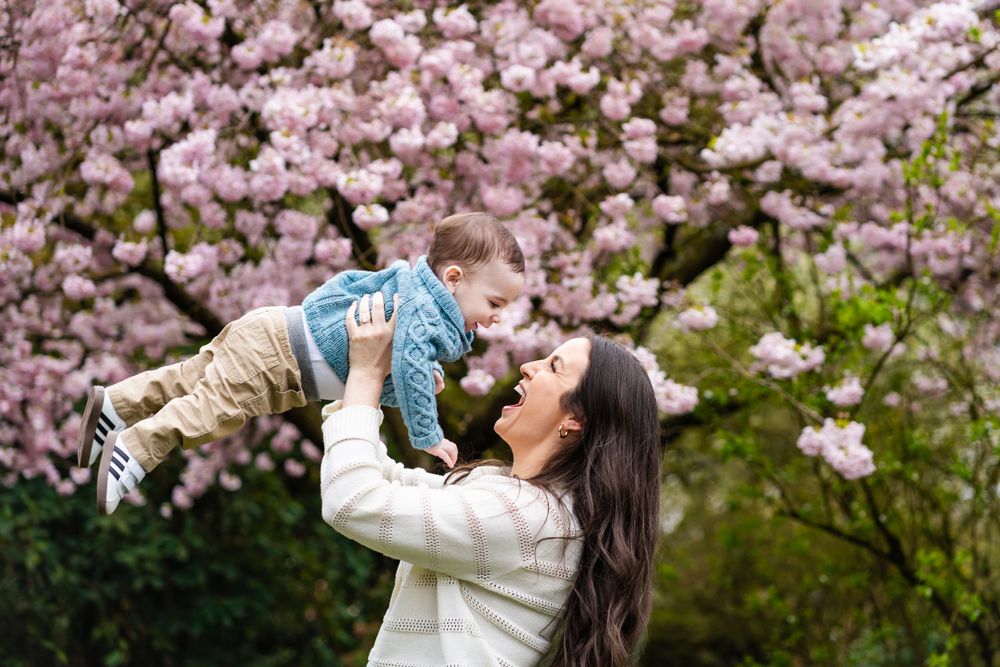 Mom holding baby in the air in front of cherry blossoms.