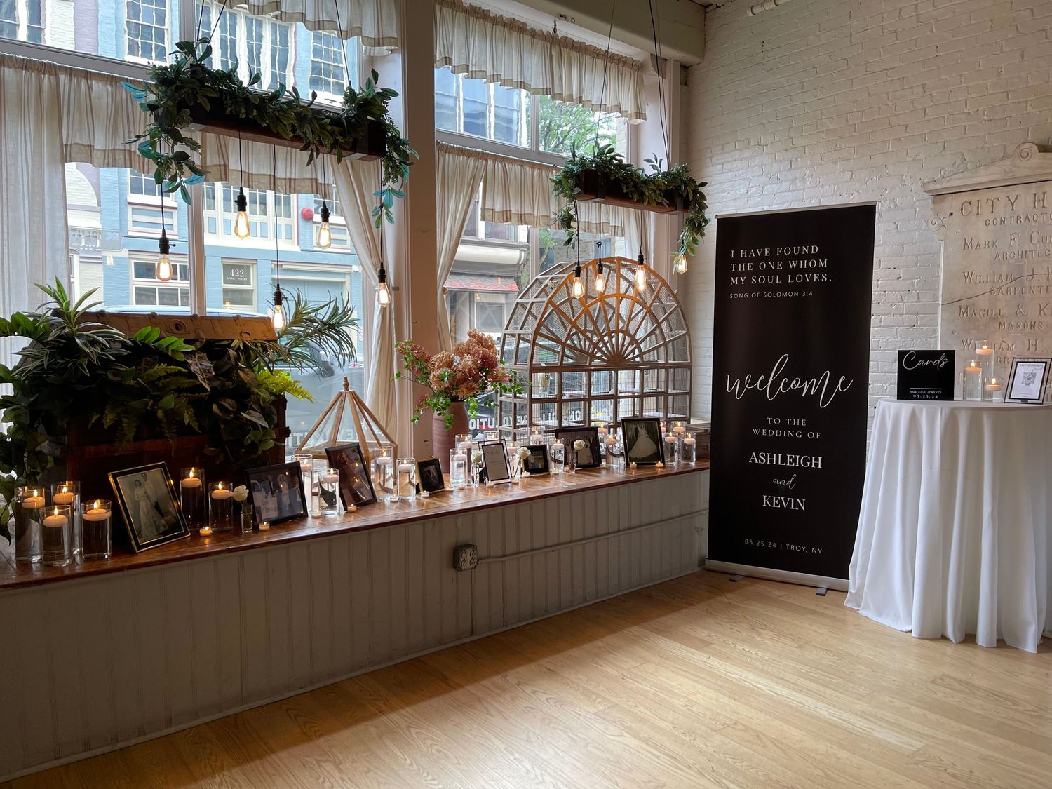 Bright wedding venue interior with wood floors, window ledge decor, and a welcome sign board in moody lighting.