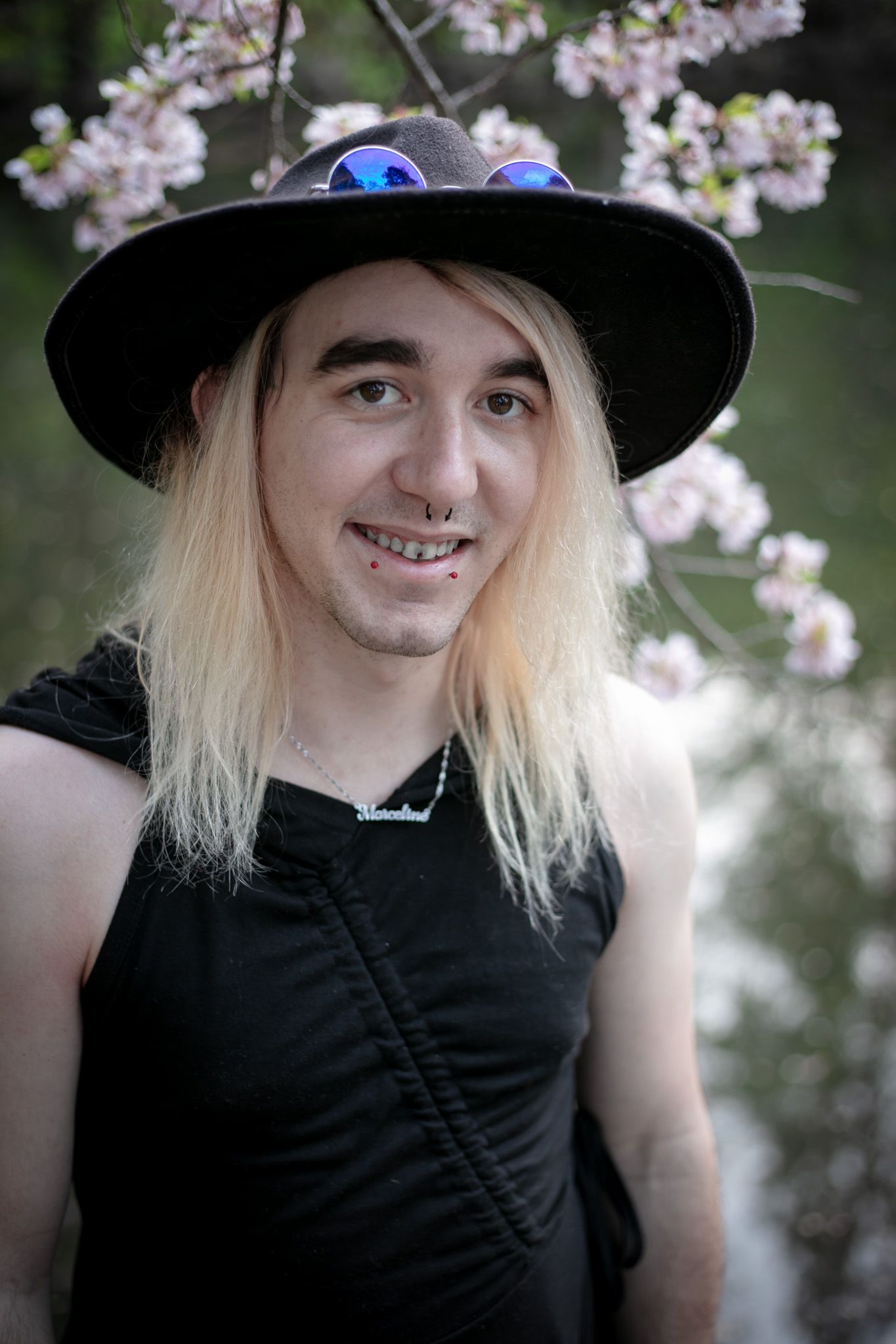 A portrait under cherry blossoms features someone in black attire and a wide-brimmed hat with sunglasses.