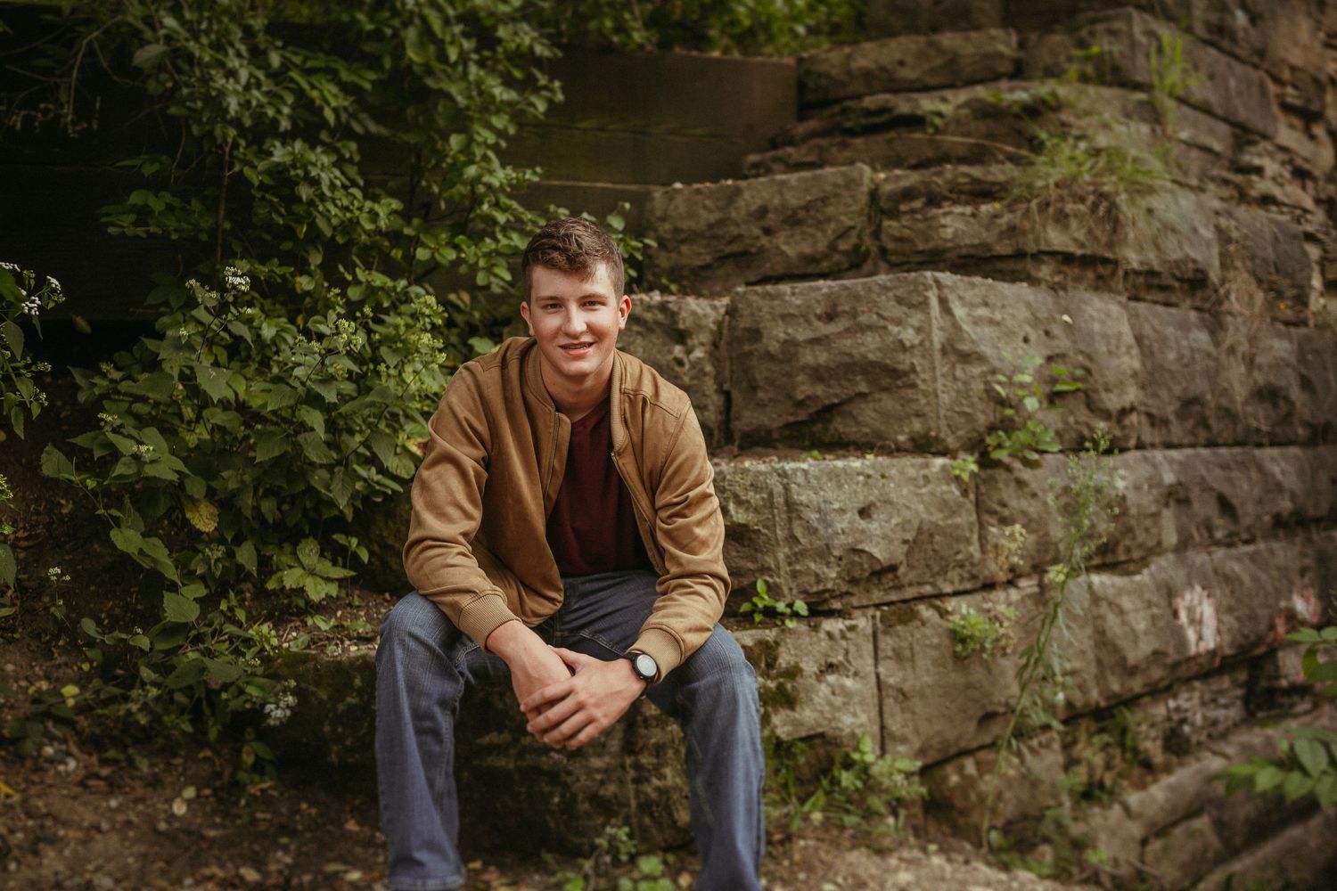 Someone sits on stone steps against a rocky wall in a casual outdoor portrait setting.