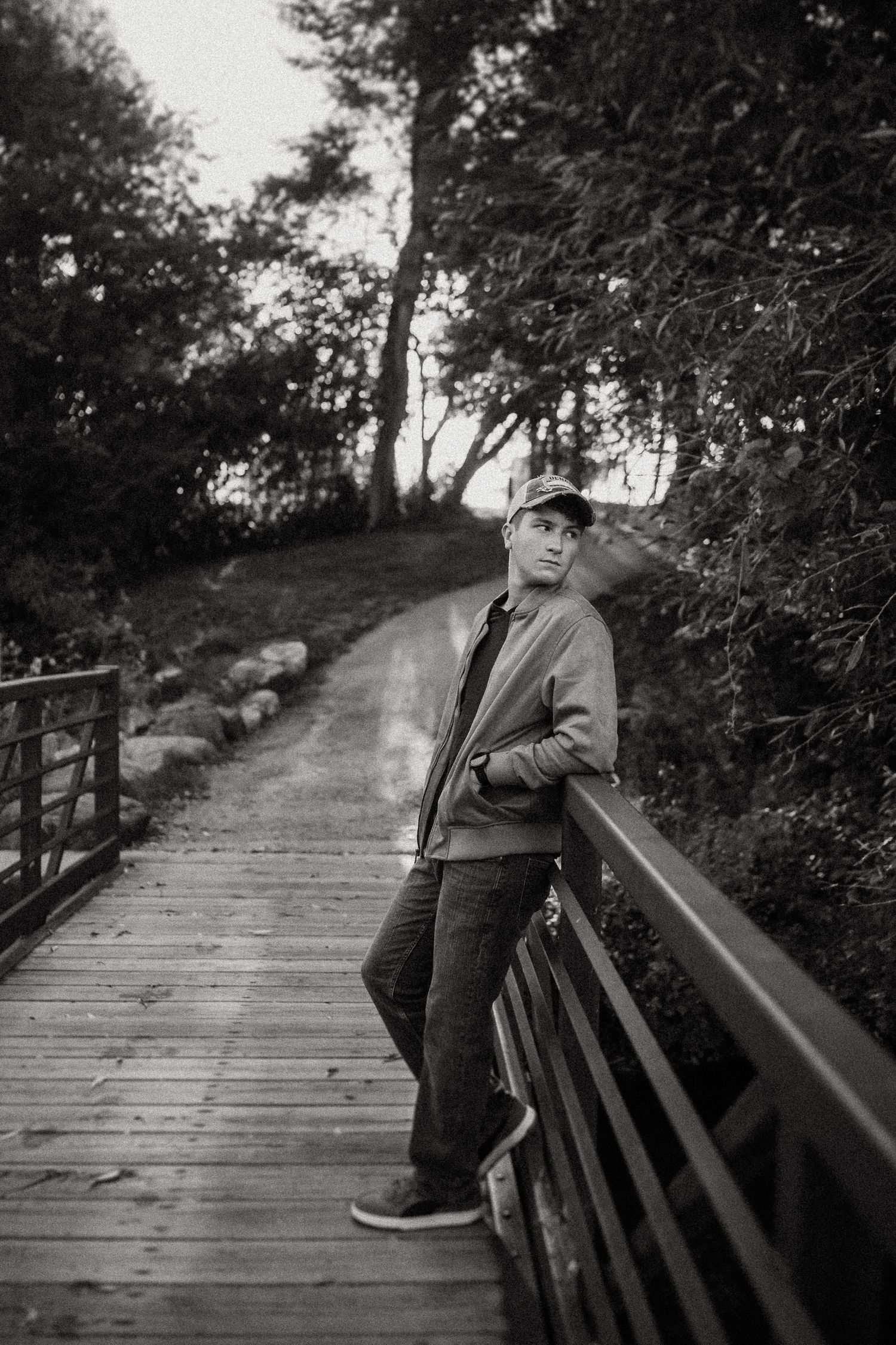 A person leans against a wooden bridge railing in a black and white forest scene.