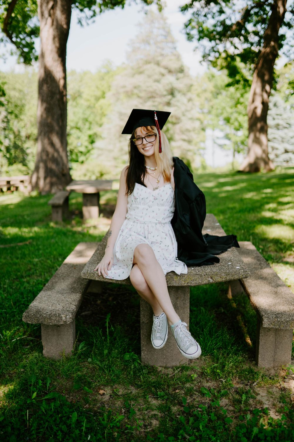 Graduation photos on a stone bench surrounded by lush green trees.