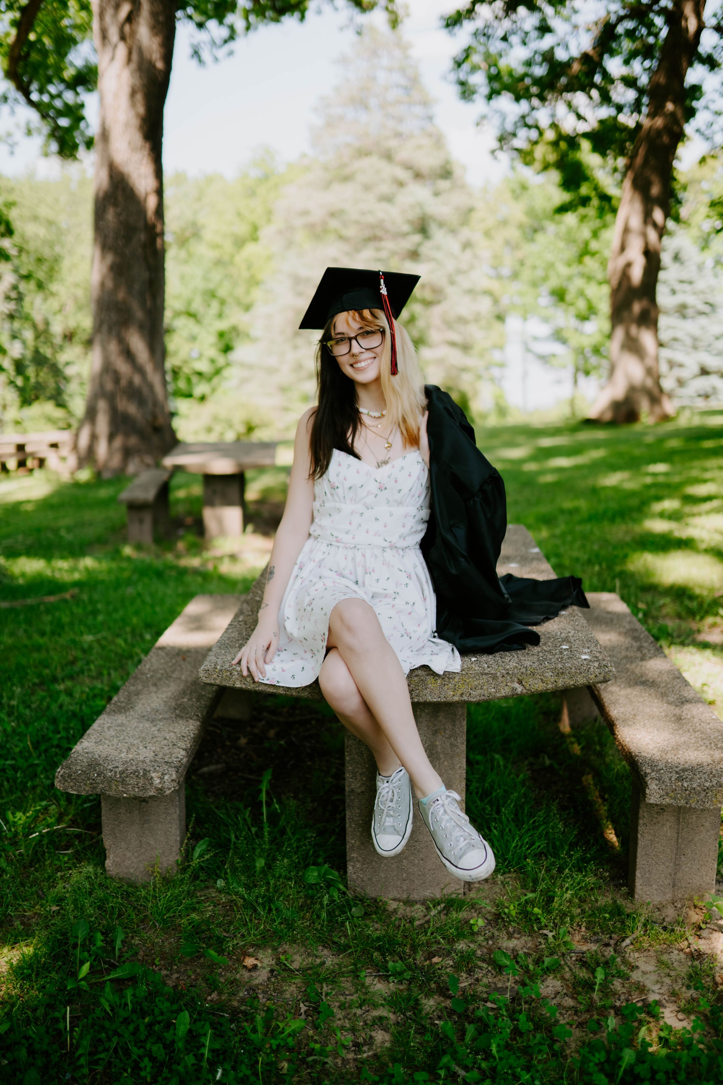 Graduation photos on a stone bench surrounded by lush green trees.
